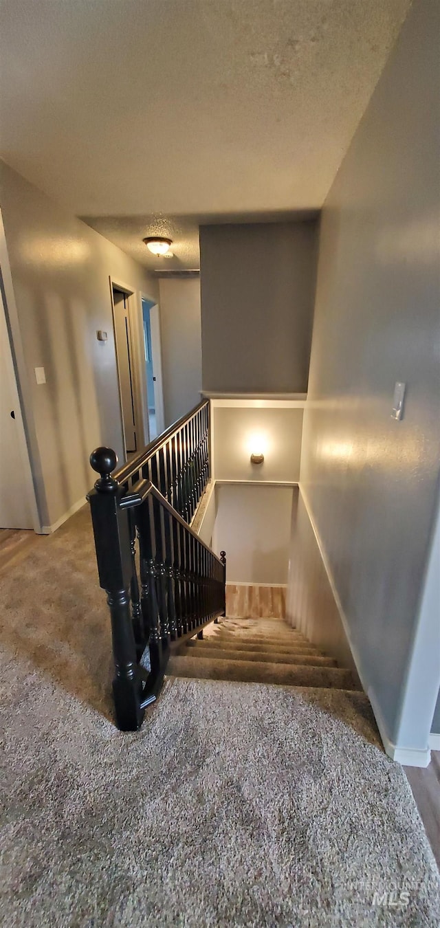 staircase with baseboards, a textured ceiling, and carpet