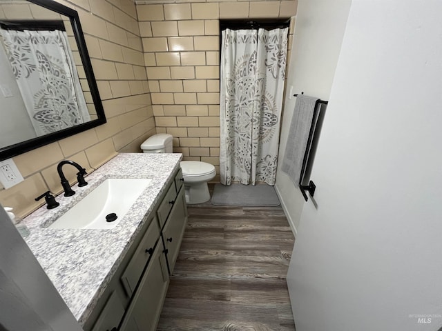bathroom featuring a shower with shower curtain, toilet, tile walls, wood finished floors, and vanity