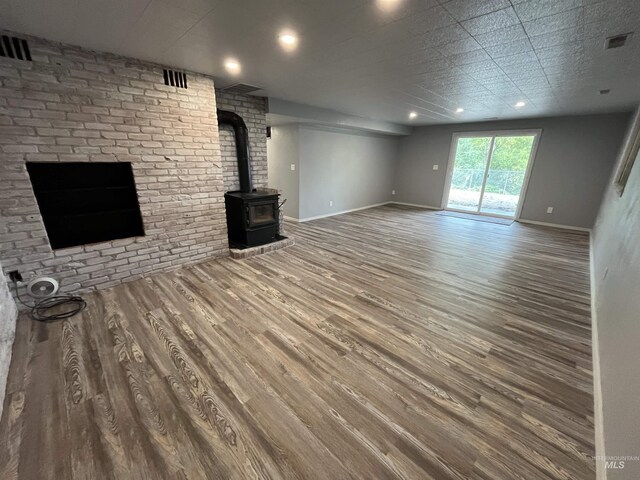 unfurnished living room with visible vents, a wood stove, wood finished floors, and baseboards