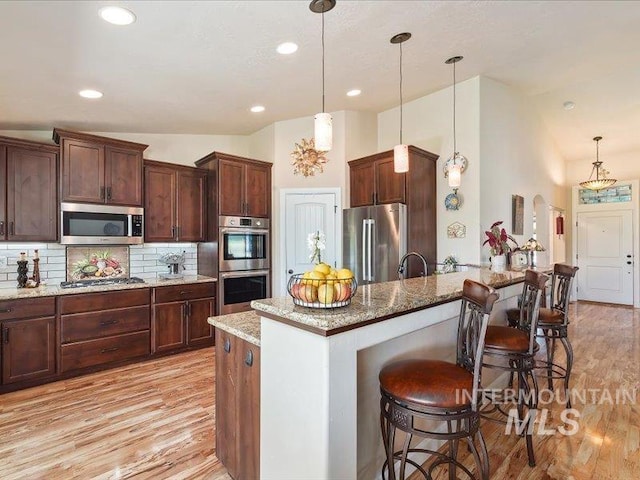 5747 W Rotherham Dr, Eagle, ID 83616 - kitchen featuring stainless steel appliances, a breakfast bar, light wood-style floors, lofted ceiling, and backsplash