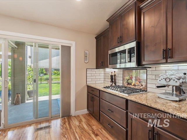 5747 W Rotherham Dr, Eagle, ID 83616 - kitchen with appliances with stainless steel finishes, tasteful backsplash, light stone counters, dark brown cabinets, and light wood-style flooring