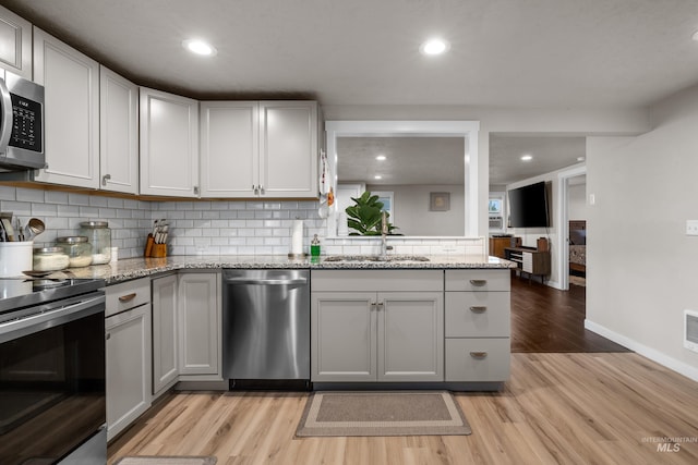 kitchen with tasteful backsplash, light hardwood / wood-style flooring, light stone counters, sink, and stainless steel appliances