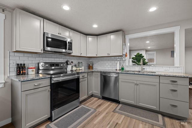 kitchen featuring appliances with stainless steel finishes, light stone counters, tasteful backsplash, and light hardwood / wood-style flooring