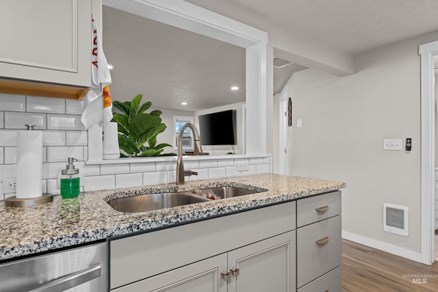 kitchen with hardwood / wood-style floors, sink, light stone countertops, stainless steel dishwasher, and white cabinetry