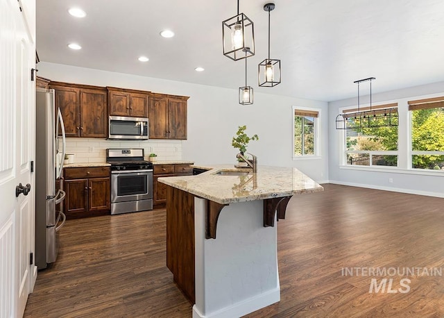 kitchen featuring light stone countertops, appliances with stainless steel finishes, tasteful backsplash, a kitchen breakfast bar, and hanging light fixtures