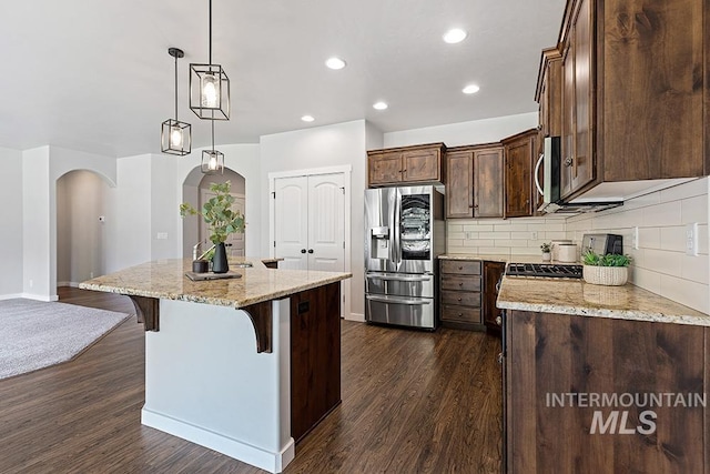 kitchen with appliances with stainless steel finishes, decorative light fixtures, a breakfast bar, light stone counters, and a center island with sink