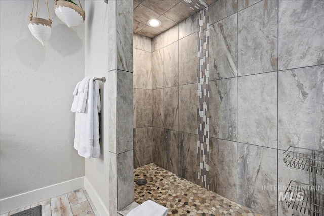 bathroom with a textured wall, baseboards, wood finished floors, and a tile shower