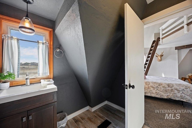 bathroom featuring connected bathroom, baseboards, wood finished floors, a textured ceiling, and a sink