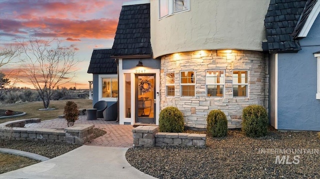 exterior entry at dusk featuring a tile roof, stone siding, and stucco siding