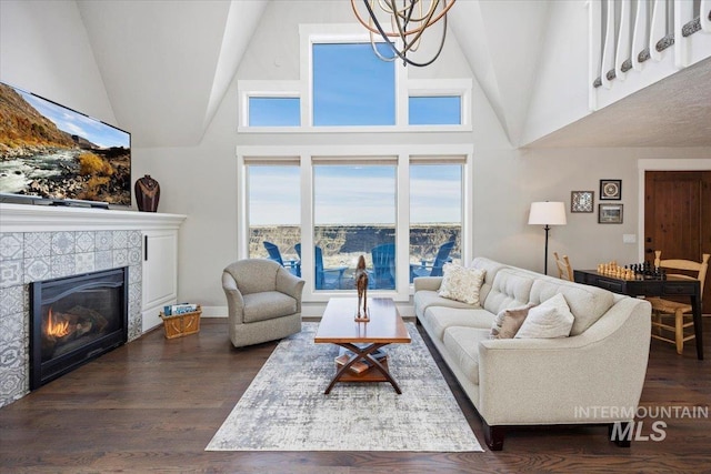 living area featuring a tiled fireplace, high vaulted ceiling, wood finished floors, and a chandelier