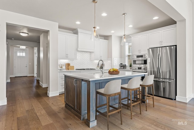 kitchen with a center island with sink, wood finished floors, appliances with stainless steel finishes, white cabinets, and light countertops