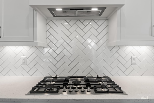 kitchen featuring ventilation hood, light stone countertops, stainless steel gas stovetop, white cabinets, and tasteful backsplash