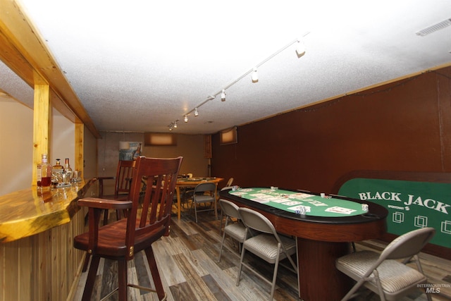 recreation room featuring bar, hardwood / wood-style flooring, rail lighting, and a textured ceiling