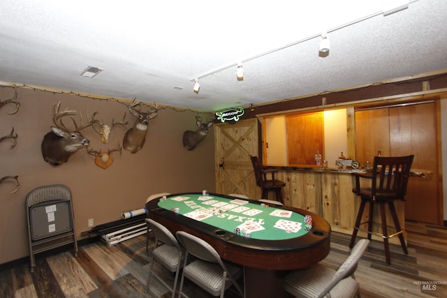 game room featuring track lighting, dark hardwood / wood-style floors, a textured ceiling, and bar area