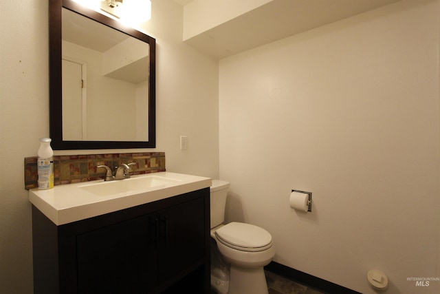 bathroom with toilet, backsplash, vanity, and baseboards