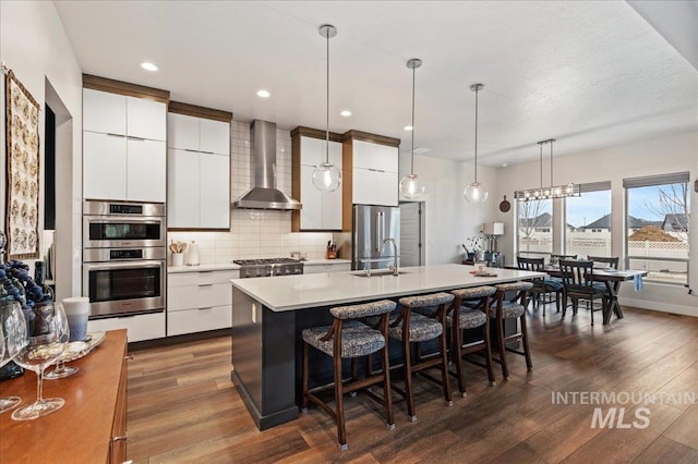 kitchen with white cabinets, stainless steel appliances, and wall chimney range hood