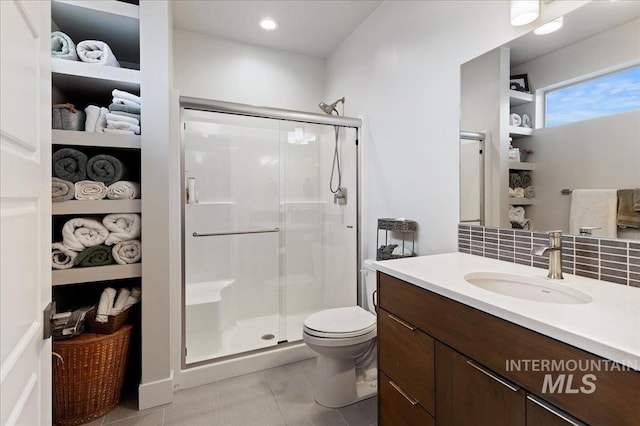 bathroom with toilet, vanity, a shower with door, tile patterned flooring, and decorative backsplash