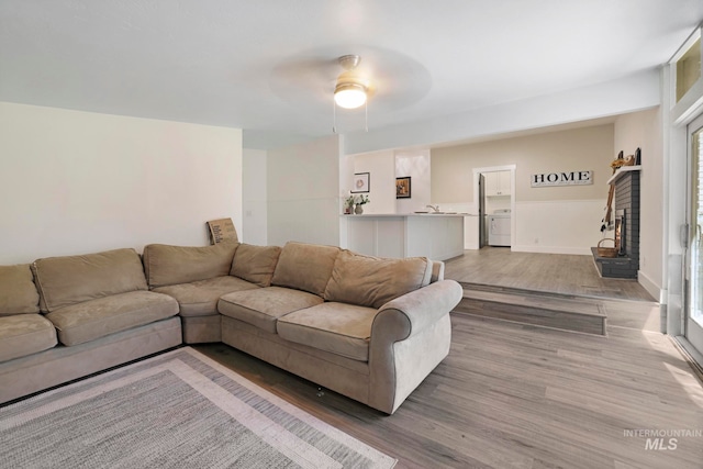 living room featuring ceiling fan, washer / dryer, light wood-type flooring, and a wealth of natural light