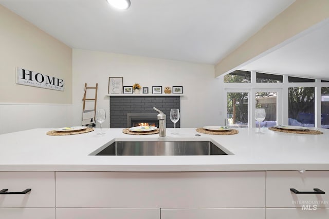 kitchen with a fireplace, white cabinetry, lofted ceiling, and sink