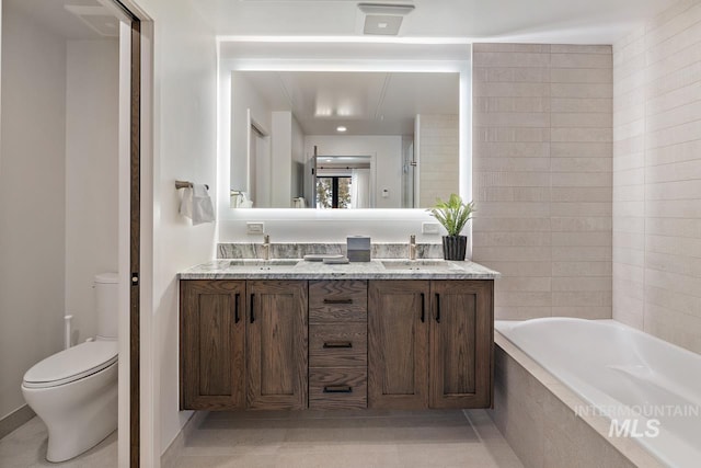 bathroom with a relaxing tiled tub, vanity, toilet, and tile patterned flooring