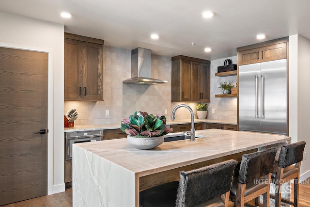 kitchen with sink, stainless steel appliances, tasteful backsplash, an island with sink, and wall chimney exhaust hood