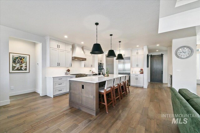 kitchen featuring light countertops, a barn door, wood finished floors, and custom range hood