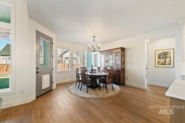 dining space with baseboards, a notable chandelier, a textured ceiling, and light wood finished floors