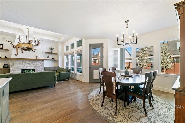 dining room with a chandelier, a textured ceiling, a fireplace, baseboards, and light wood-style floors