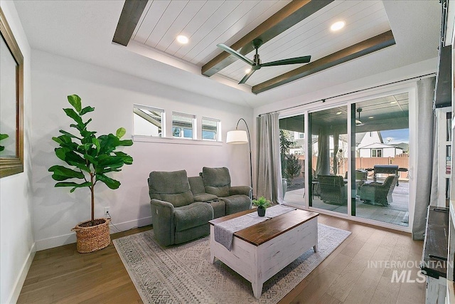 living room featuring a tray ceiling, beamed ceiling, baseboards, and wood finished floors