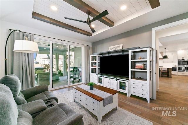 living area with wooden ceiling, a ceiling fan, a raised ceiling, and wood finished floors