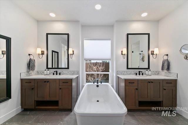 full bathroom featuring two vanities, a soaking tub, and a sink