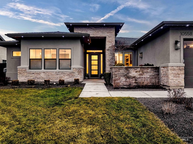 exterior space featuring an attached garage, stone siding, a lawn, and stucco siding