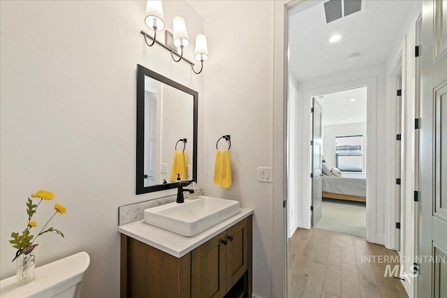 ensuite bathroom with visible vents, connected bathroom, toilet, wood finished floors, and vanity