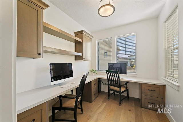 office space with light wood-type flooring, built in study area, a textured ceiling, and baseboards