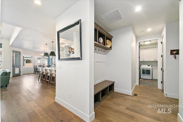 corridor with washer / dryer, hardwood / wood-style flooring, visible vents, and baseboards