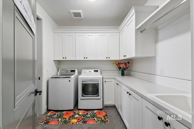 clothes washing area featuring cabinet space, visible vents, a sink, a textured ceiling, and independent washer and dryer