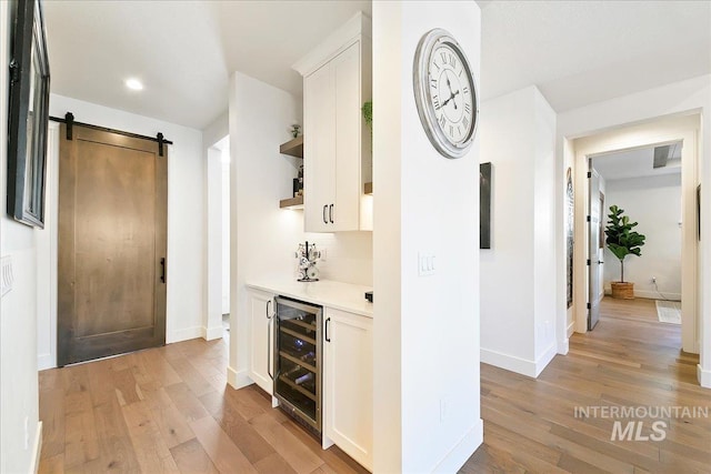 corridor featuring light wood-type flooring, beverage cooler, baseboards, and a barn door