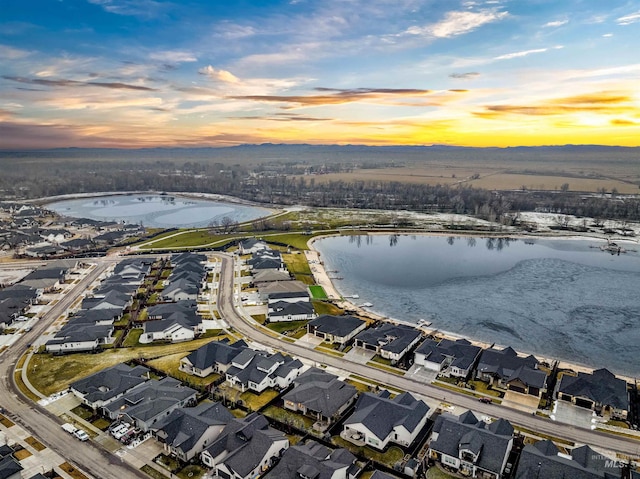 aerial view at dusk with a water view and a residential view