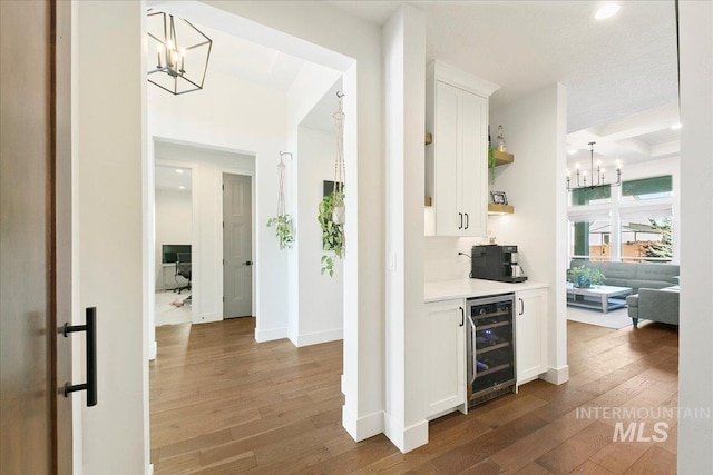 hall with a chandelier, wine cooler, wood-type flooring, and baseboards