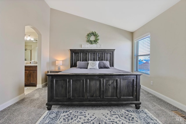 carpeted bedroom with connected bathroom, vaulted ceiling, and sink