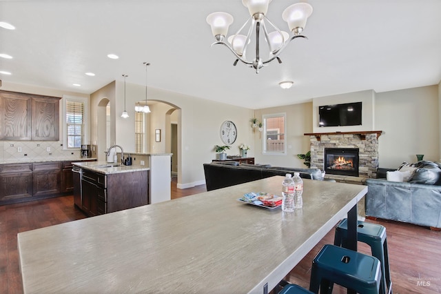 dining area with a notable chandelier, dark hardwood / wood-style flooring, a stone fireplace, and sink