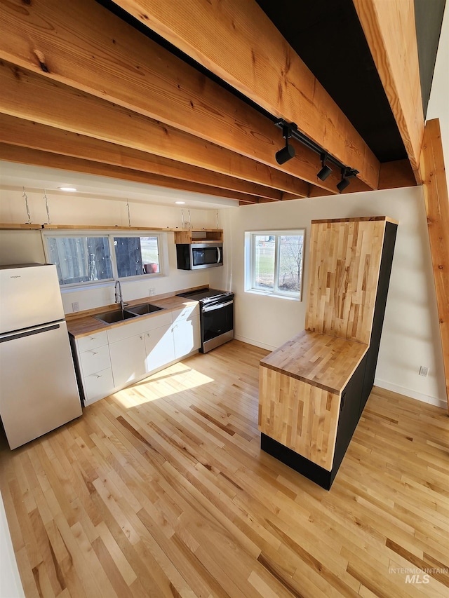 kitchen featuring light wood finished floors, beam ceiling, appliances with stainless steel finishes, and a sink