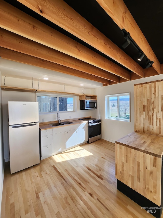 kitchen featuring appliances with stainless steel finishes, beam ceiling, a sink, and light wood finished floors