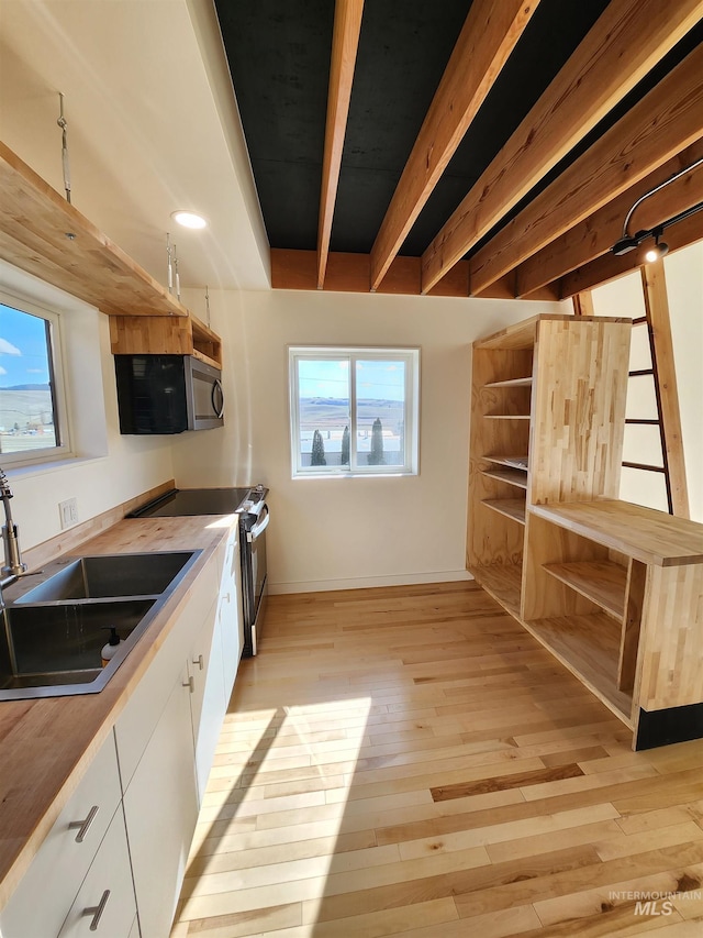 kitchen featuring stainless steel microwave, light wood-style flooring, a sink, range with electric cooktop, and beamed ceiling