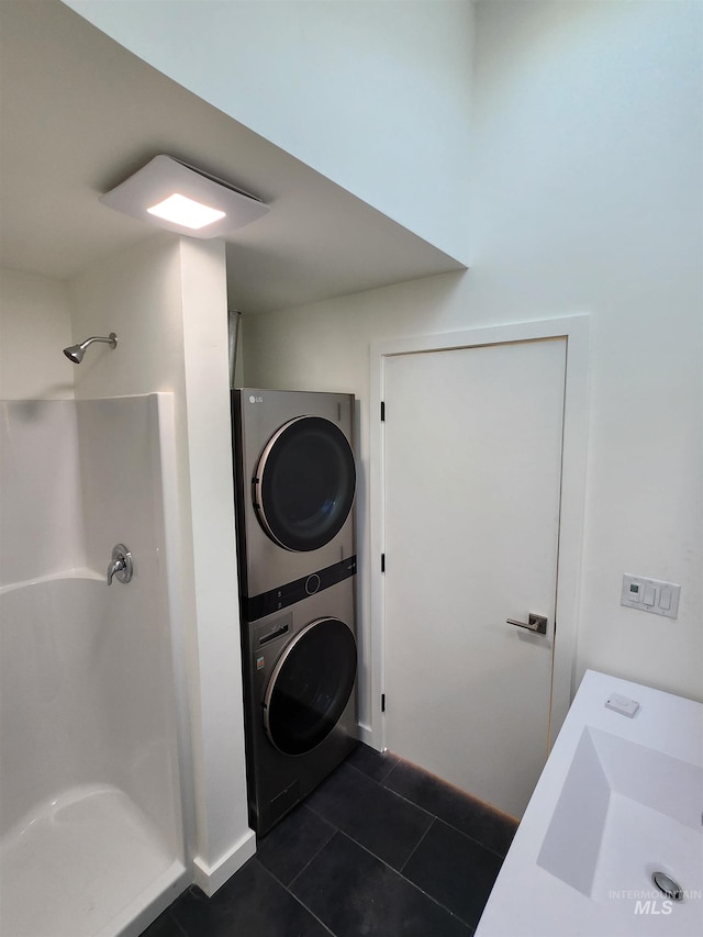 laundry area featuring stacked washer / dryer, laundry area, a sink, and dark tile patterned floors