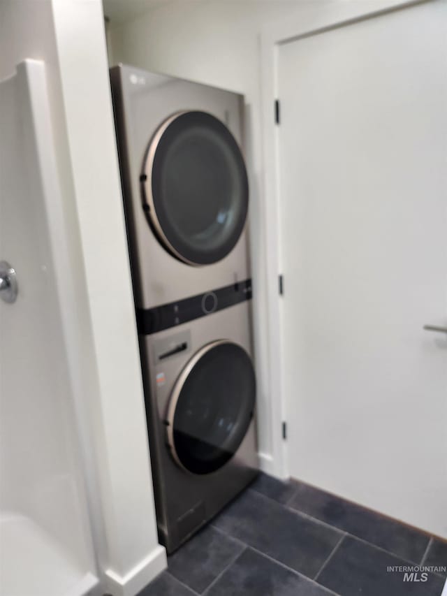 laundry room featuring laundry area, dark tile patterned floors, and stacked washer / drying machine