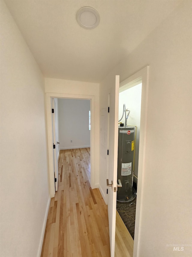 corridor featuring light wood finished floors, water heater, and baseboards