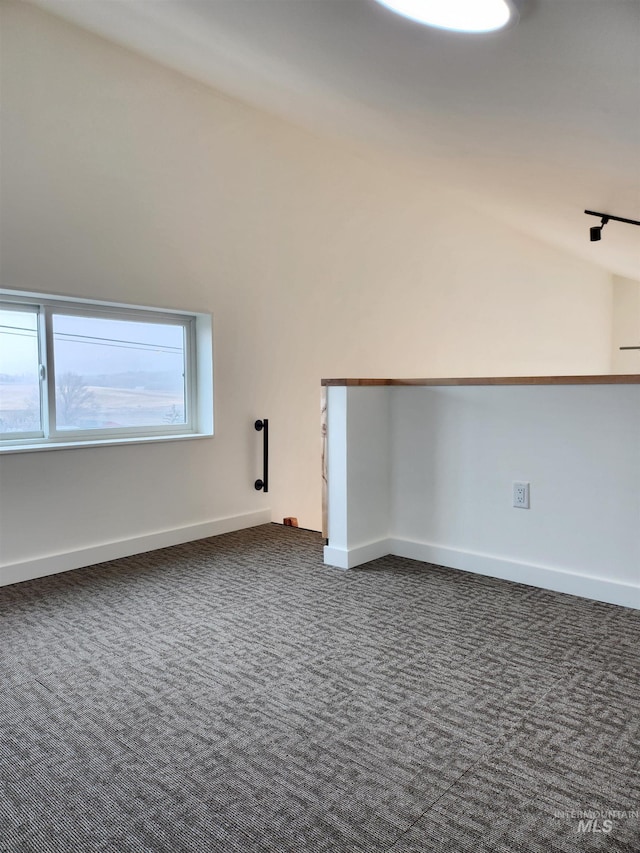 spare room featuring vaulted ceiling, dark colored carpet, and baseboards