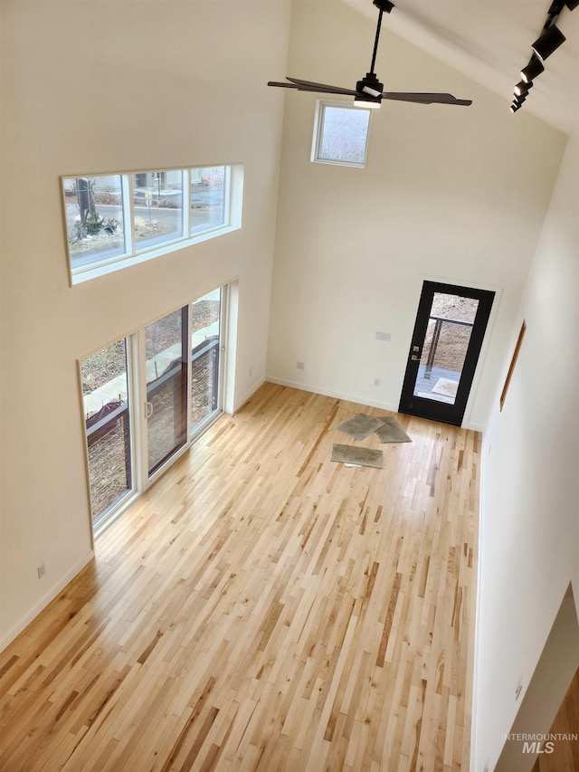 unfurnished living room with high vaulted ceiling, light wood-type flooring, baseboards, and a ceiling fan