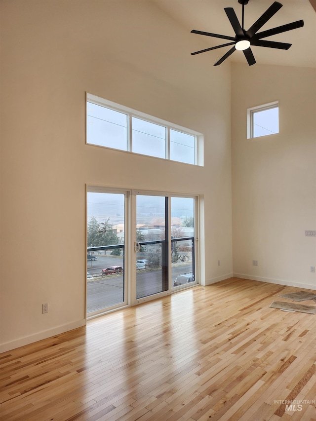 unfurnished room with a towering ceiling, light wood-style flooring, and baseboards